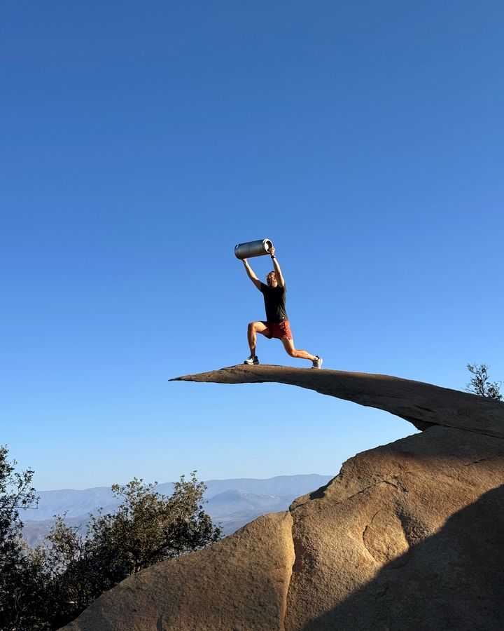 A Perpetual founder lifting a Superfood Company kombucha keg overhead at the tip of Potato Chip Rock in Poway, near Scripps Ranch
